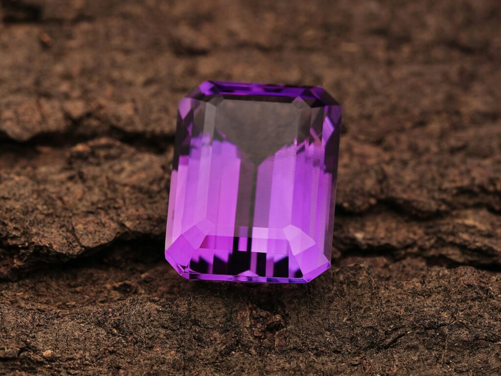 Close-up of a radiant purple amethyst gemstone placed on a rugged textured surface, highlighting its clarity and cut.
