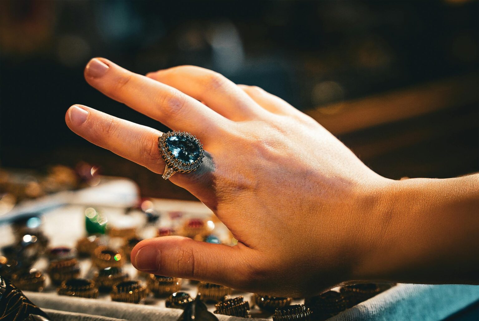 A close-up of a hand showcasing an ornate sapphire diamond ring in a jewelry setting.