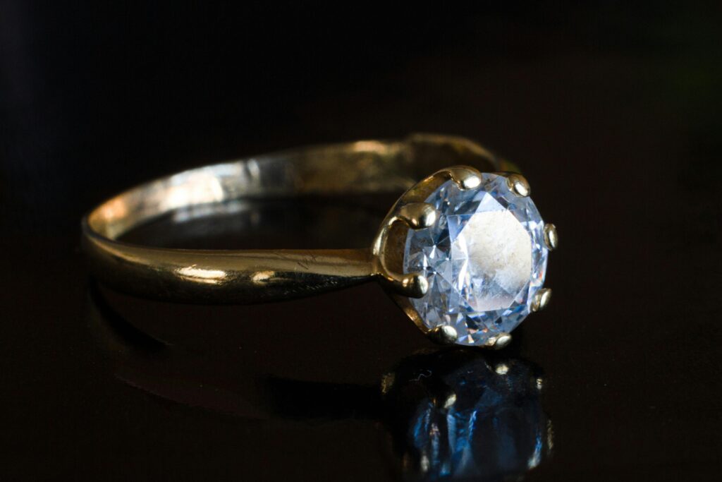 Close-up of a beautiful solitaire diamond ring with a golden band displayed against a black backdrop.