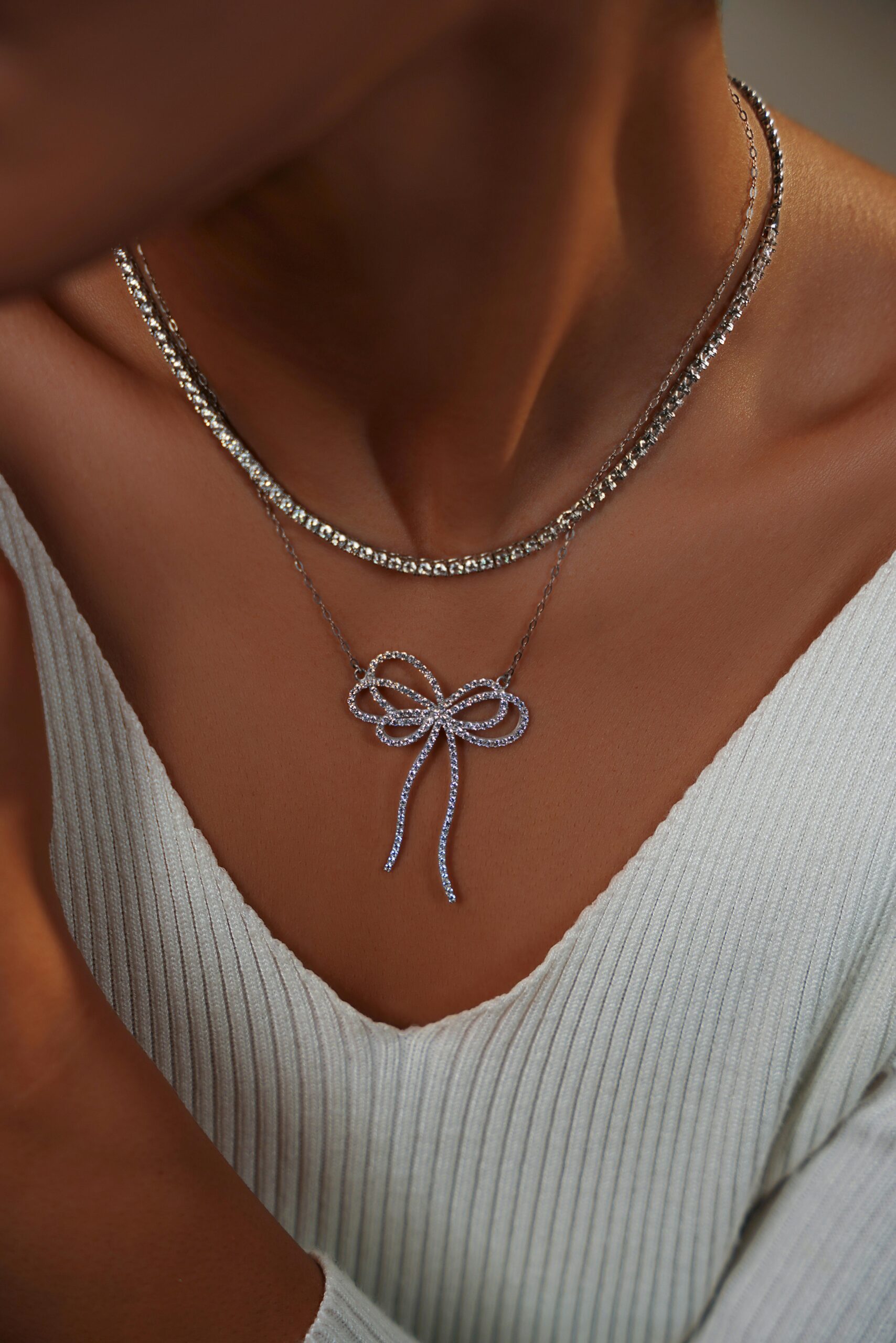 Close-up of a diamond bow pendant necklace on a woman wearing a white sweater.