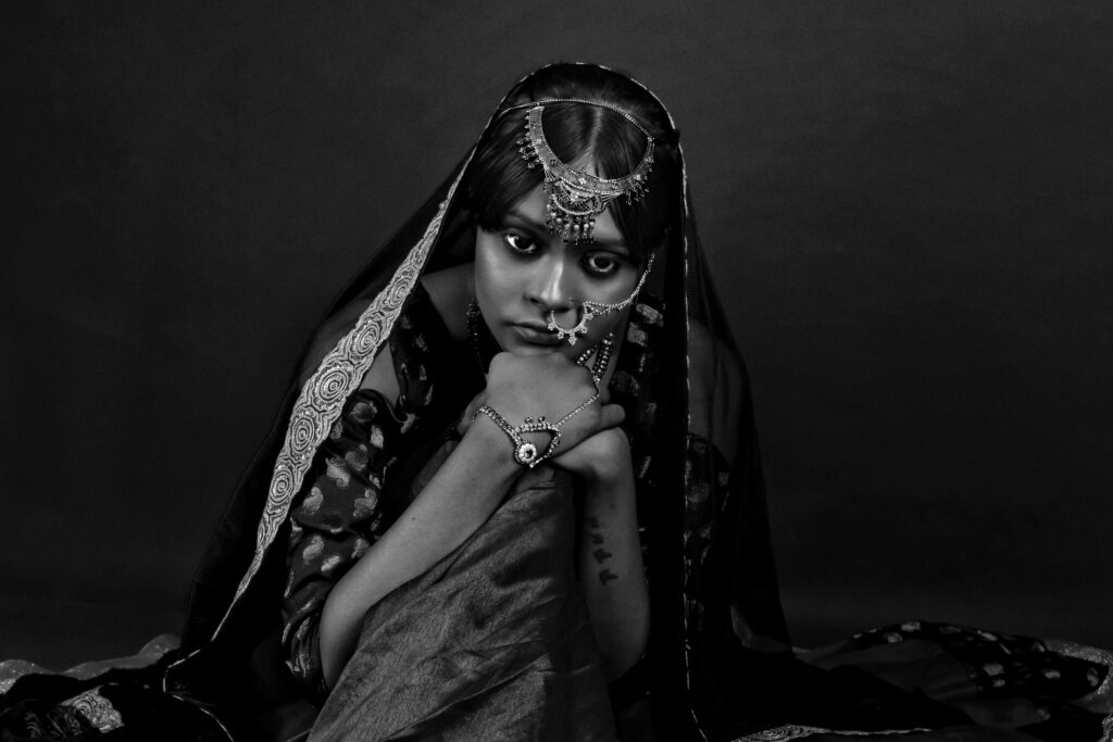 Striking black and white portrait of a woman adorned with traditional Indian jewelry, expressing deep emotion.