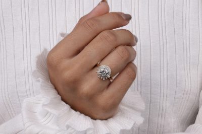 Close-up shot of a woman's hand wearing a diamond ring against a white blouse.